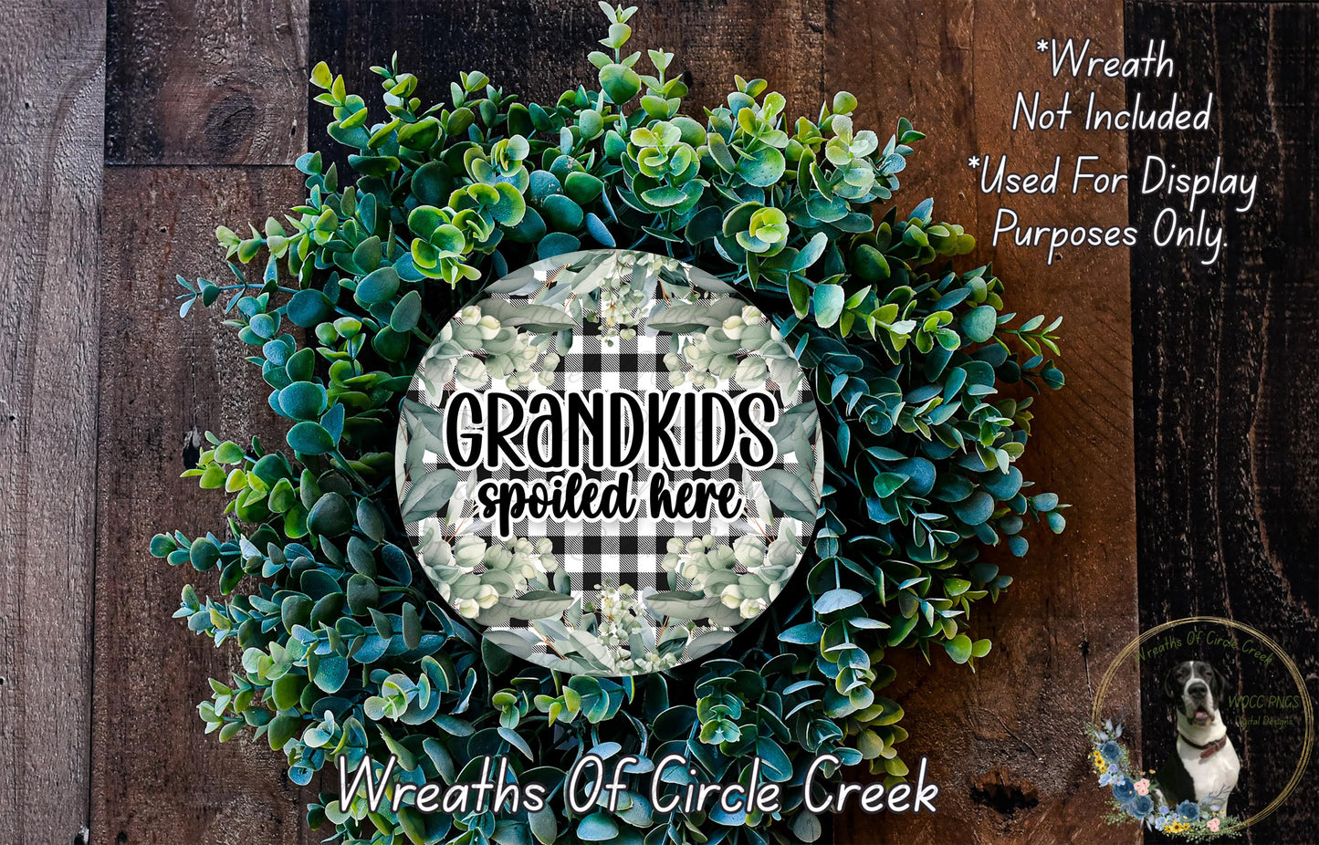 a wreath made of green succulent plants, with a circular sign in the center that says "Grandkids spoiled here". The wreath is displayed on a wooden surface, and there is a small dog in the bottom right corner.