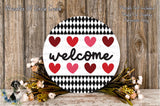 a round sign with the word "welcome" written on it, surrounded by a wreath of flowers and a wooden background.
