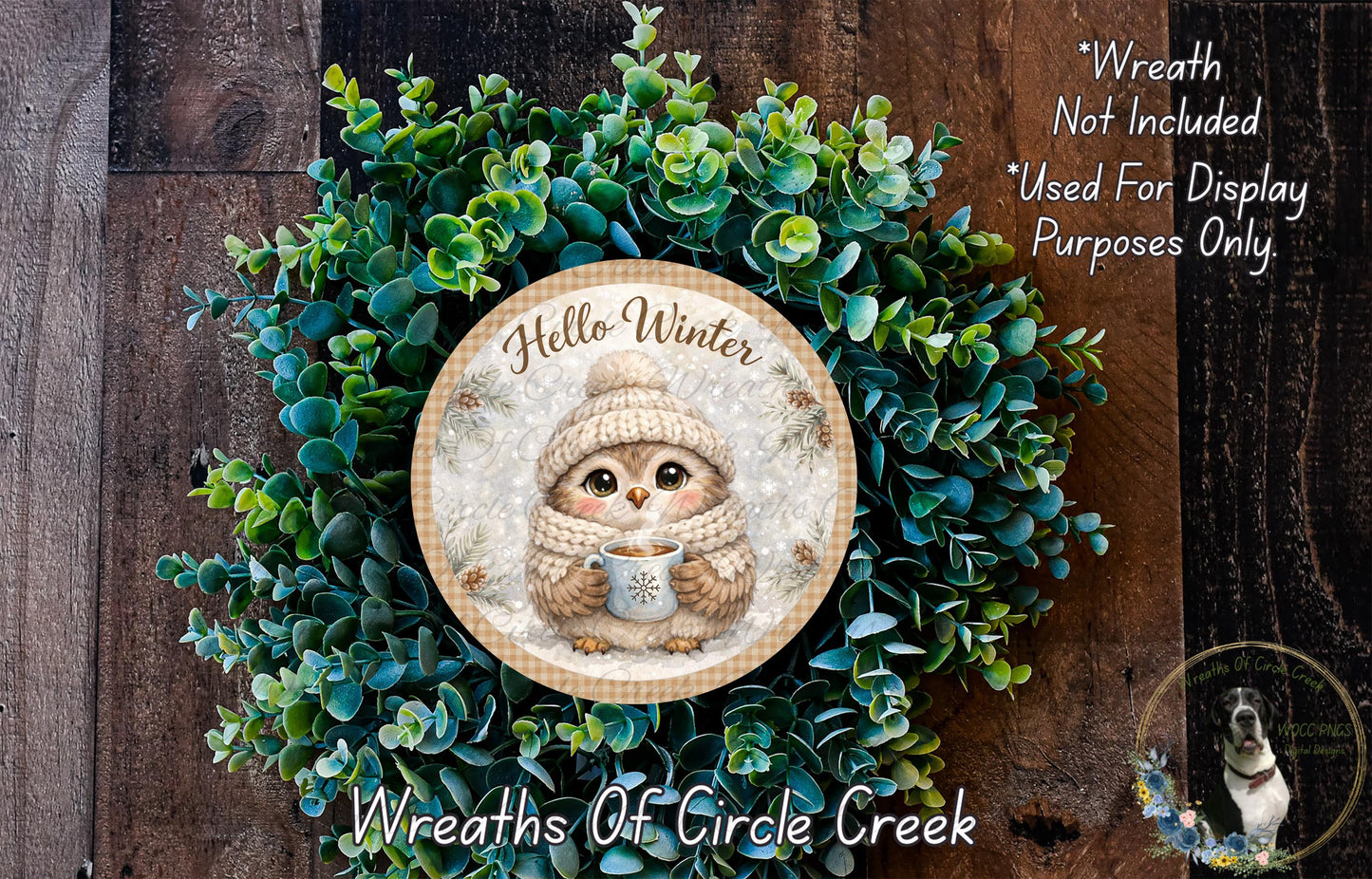 A wreath with a cute owl wearing a winter hat and scarf, surrounded by green foliage. The wreath is displayed on a wooden surface.
