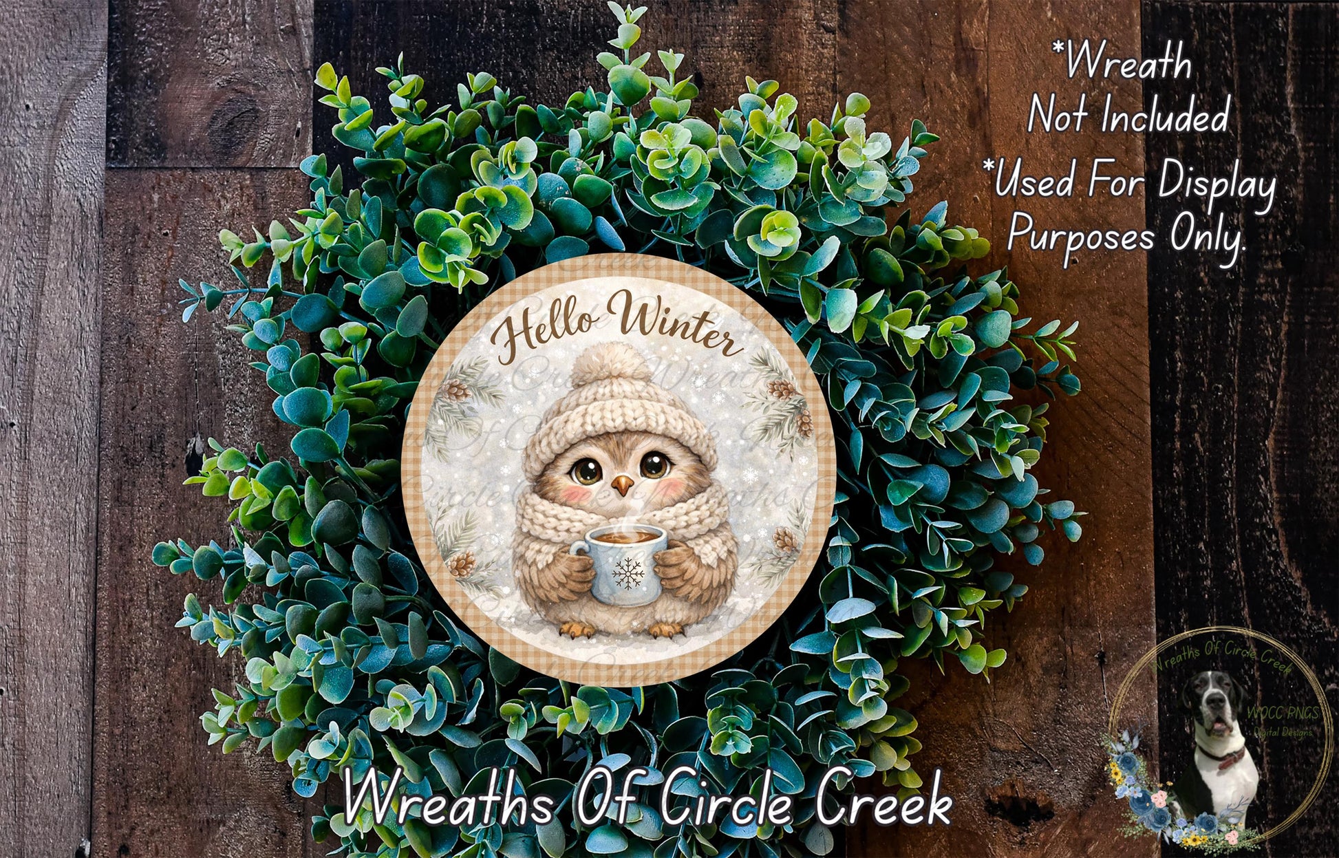 A wreath with a cute owl wearing a winter hat and scarf, surrounded by green foliage. The wreath is displayed on a wooden surface.