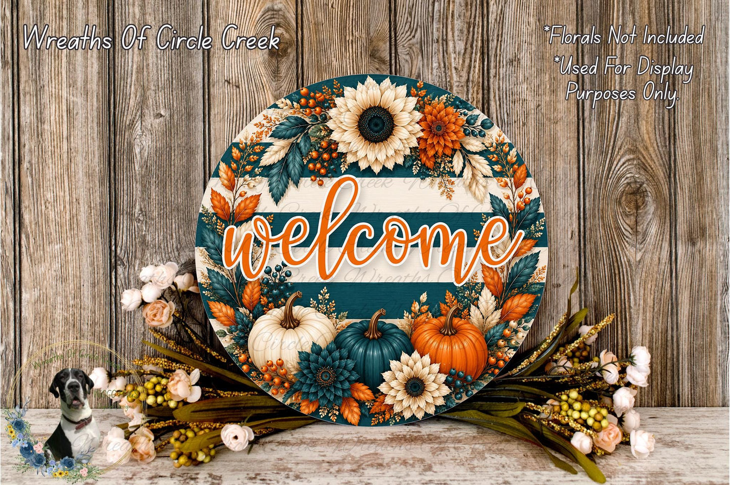 a decorative welcome sign with a floral design, surrounded by autumn-themed elements such as pumpkins, flowers, and leaves. The sign is placed on a wooden surface, and there is a small bird figurine in the background.