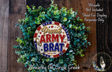 a wreath made of green leaves and a circular emblem with the text "Proud Army Brat" on it. The wreath is displayed on a wooden surface, and there is a small dog in the bottom right corner of the image.