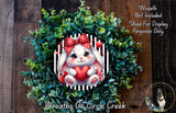 A wreath made of green leaves and a white rabbit with a red bow, holding a red heart, is displayed on a wooden surface.
