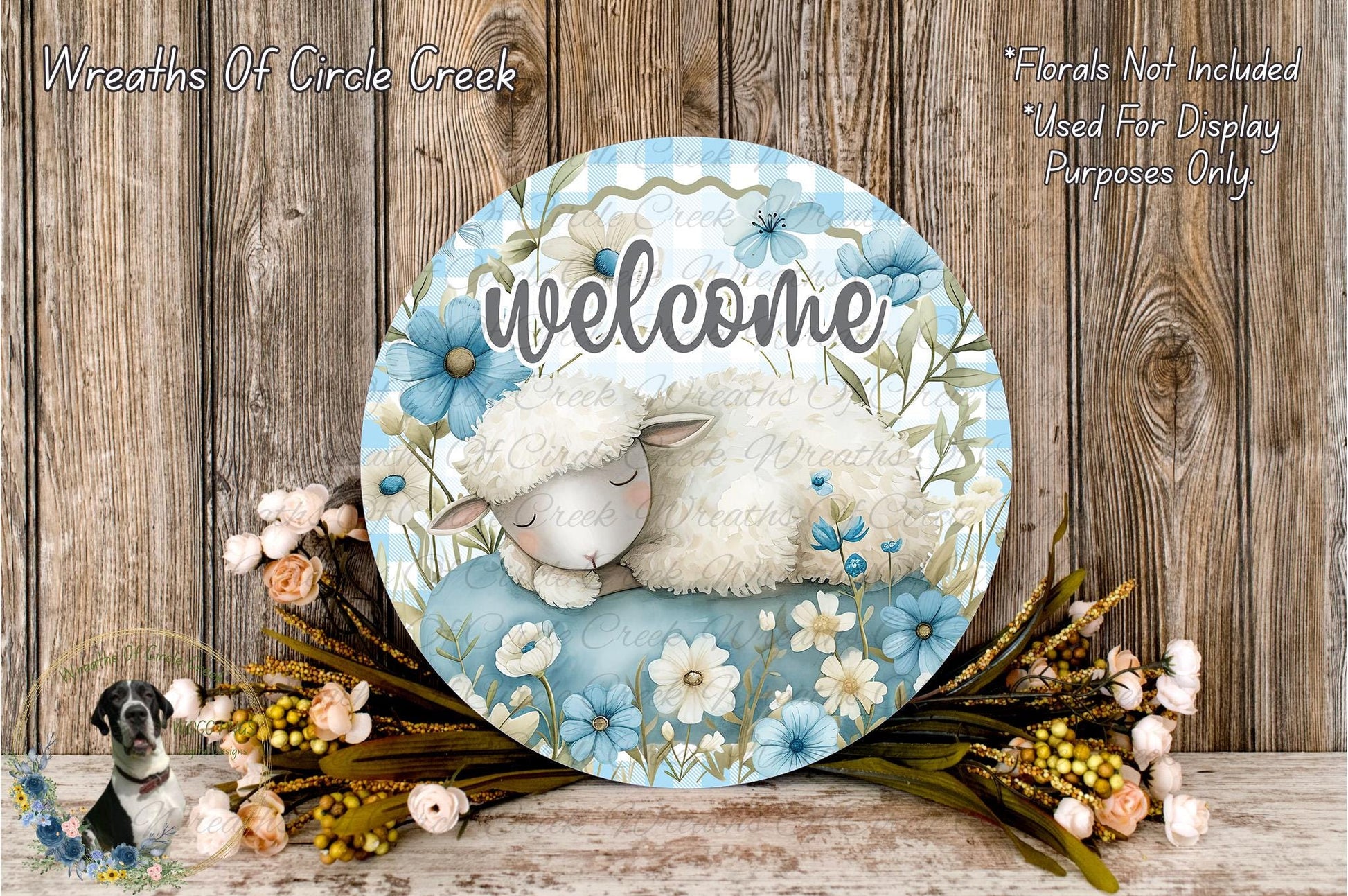 A decorative welcome sign with a sleeping lamb and flowers, placed on a wooden surface.