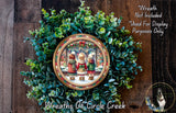 A wreath with a picture of three people in winter clothing, surrounded by greenery, hangs on a wooden wall.