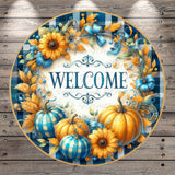 A decorative welcome sign featuring a blue and white plaid border, surrounded by a wreath of autumn leaves and flowers, with pumpkins and sunflowers.