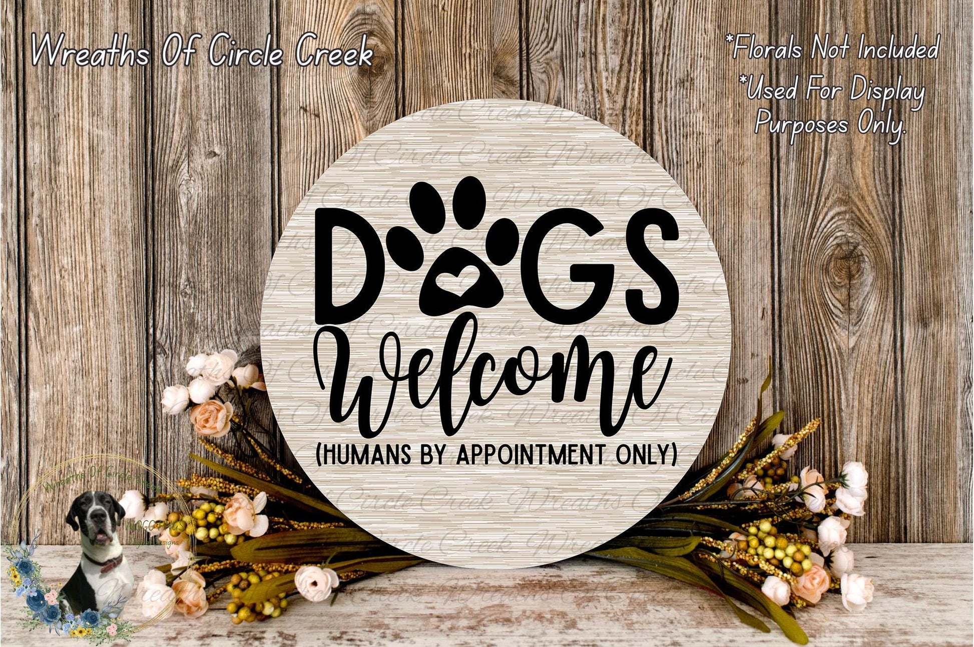 a wooden sign with the text "Dogs Welcome" and a paw print, surrounded by a floral arrangement and a wooden wall.