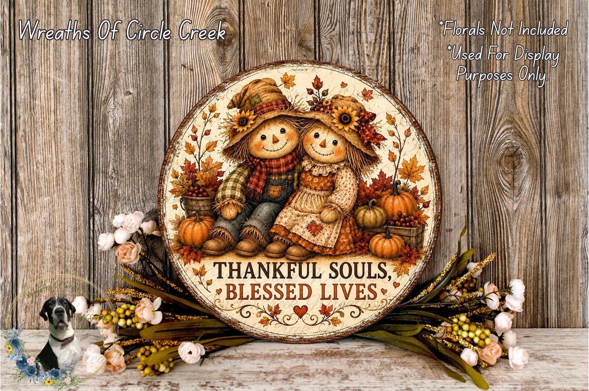 a round wooden plaque with a painting of two scarecrow figures, surrounded by autumn decorations such as pumpkins and flowers. The plaque has a message that reads "Thankful Souls, Blessed Lives".