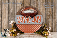 a wooden sign with the text "game day" and a football, surrounded by a floral arrangement and a wooden background.