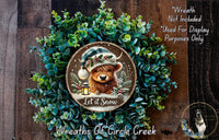 A wreath made of green plants and a brown bear wearing a Santa hat, with the text "Let it Snow" and "Wreaths of Circle Creek" displayed.