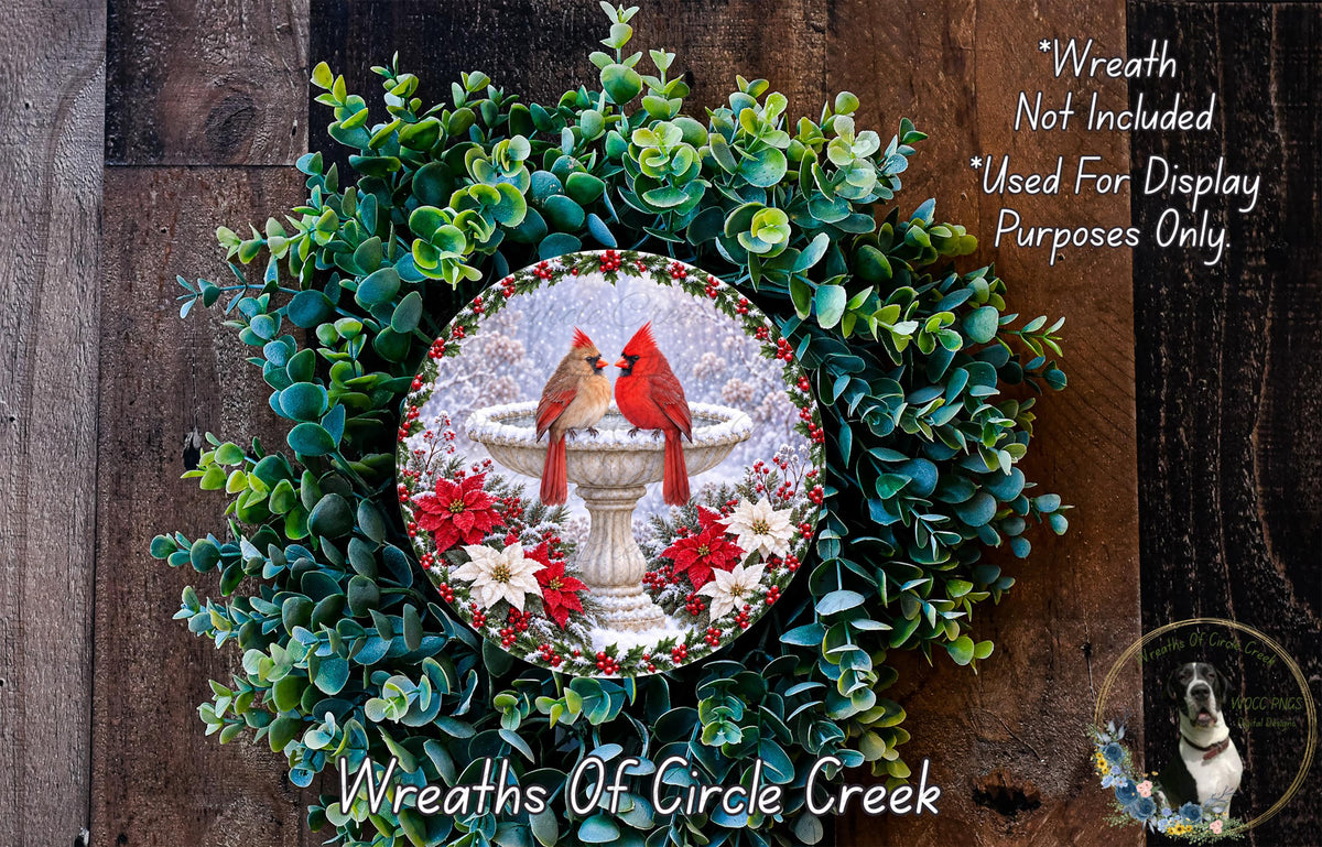 A wreath made of green leaves and red poinsettias, featuring a white bird bath with two red birds perched on it. The wreath is displayed on a wooden wall, and there is a small dog in the bottom right corner.