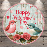 A circular graphic with a wooden background, featuring two birds, pink and blue, and pink and red hearts. The text "Happy Valentine's Day" is displayed in the center of the image.