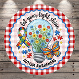 A round sign with a checkered border and a light bulb containing flowers, surrounded by puzzle pieces and a butterfly. The sign features a message about Autism Awareness.