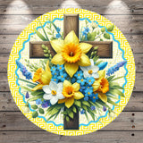 A circular arrangement of a wooden cross surrounded by a vibrant bouquet of yellow and blue flowers, including daffodils and forget-me-nots, against a yellow and blue geometric patterned background.