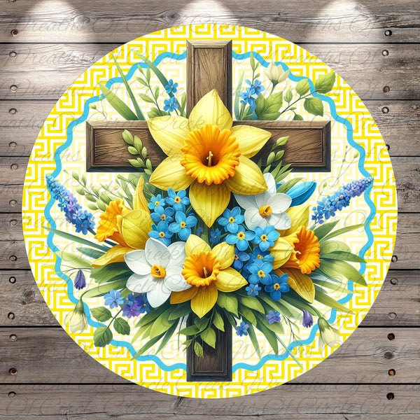 A circular arrangement of a wooden cross surrounded by a vibrant bouquet of yellow and blue flowers, including daffodils and forget-me-nots, against a yellow and blue geometric patterned background.