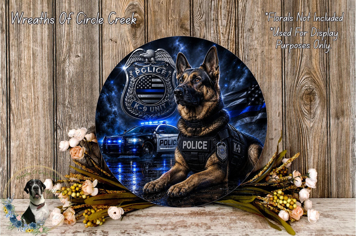 a German Shepherd police dog wearing a police vest, sitting in front of a police car with a police emblem on the hood. The dog is positioned in front of a floral arrangement, and there is a text overlay that reads "Wreaths Of Circle Creek" and "Flowers Not Included Used For Display Purposes Only".