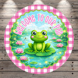 A round sign with a cartoon frog sitting on a lily pad in a pond, surrounded by pink flowers and green lily pads. The sign has a pink and white checkered border and the text "Welcome to our pad" written above the frog.