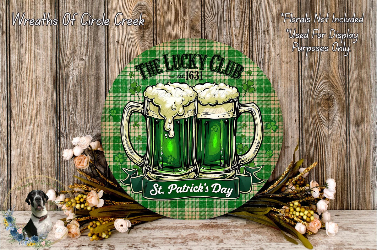 a circular sign with a green plaid background and a depiction of two green beer mugs with frothy white tops, surrounded by flowers and greenery. The sign reads "The Lucky Club St. Patrick's Day" and is placed on a wooden surface.
