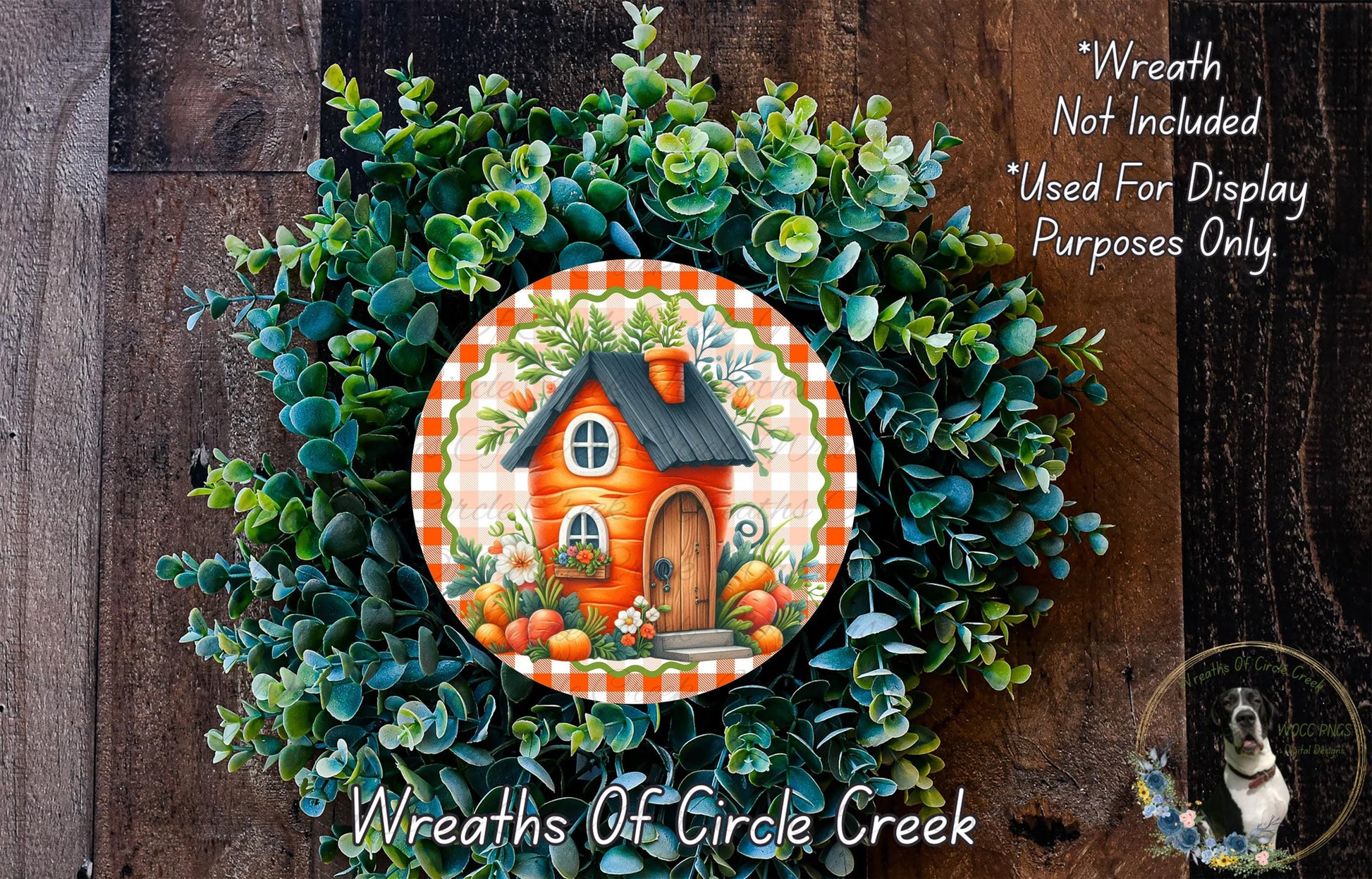 a wreath with a house and greenery, including a small orange house, on a wooden background.