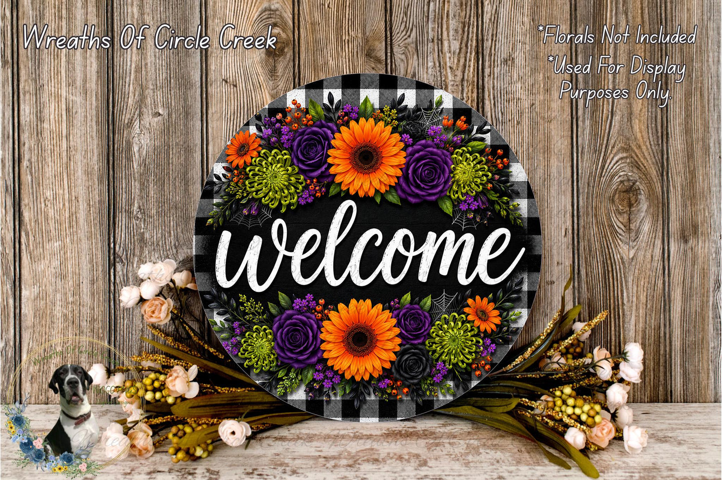 a decorative welcome sign with a floral arrangement, placed on a wooden surface. The sign is surrounded by various flowers, including sunflowers, roses, and other colorful blooms. The background is a wooden wall with a rustic, natural appearance.