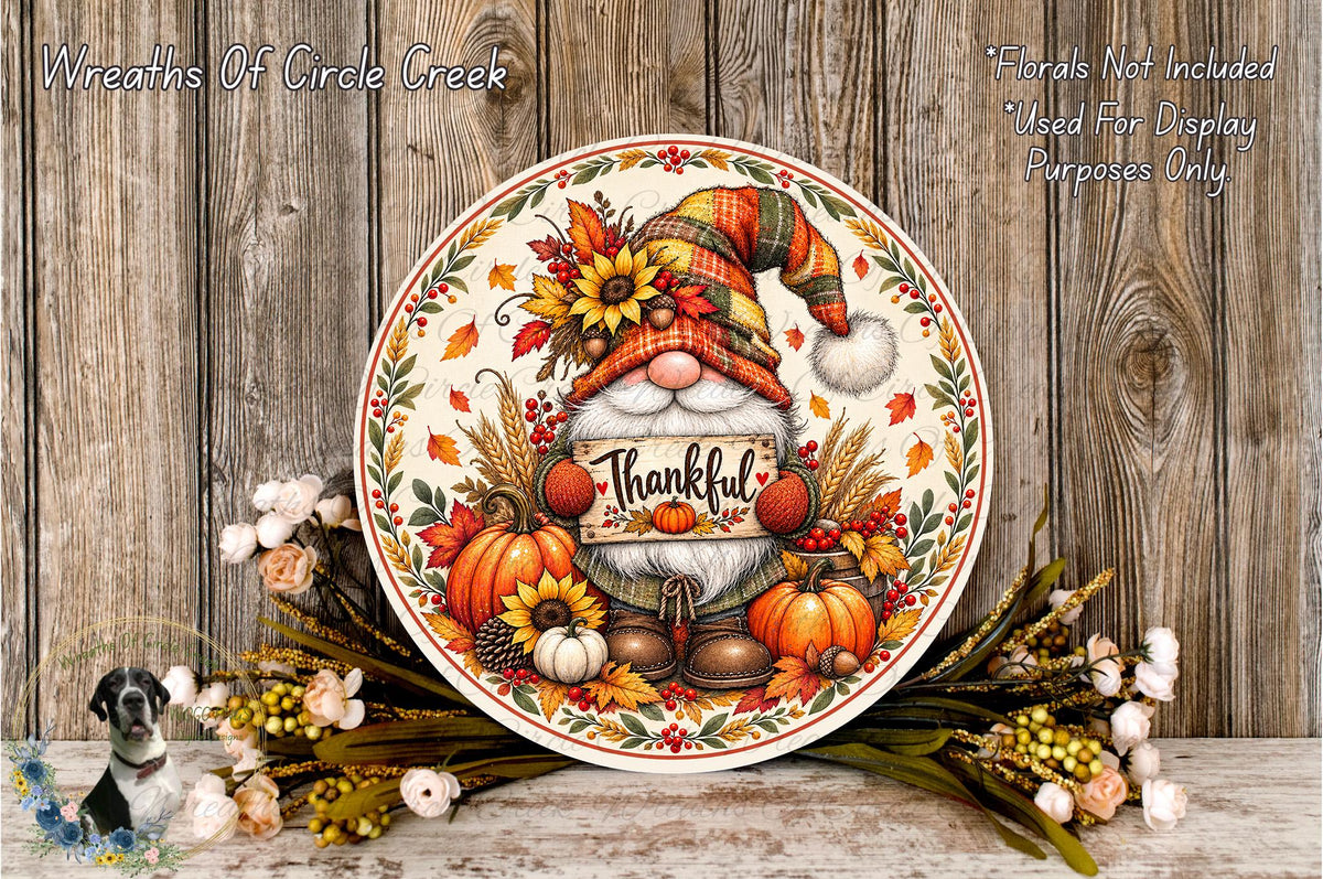 A decorative wreath with a gnome holding a "Thankful" sign, surrounded by autumn-themed elements such as pumpkins, sunflowers, and pine cones. The wreath is placed on a wooden surface, and there are additional floral elements in the background.