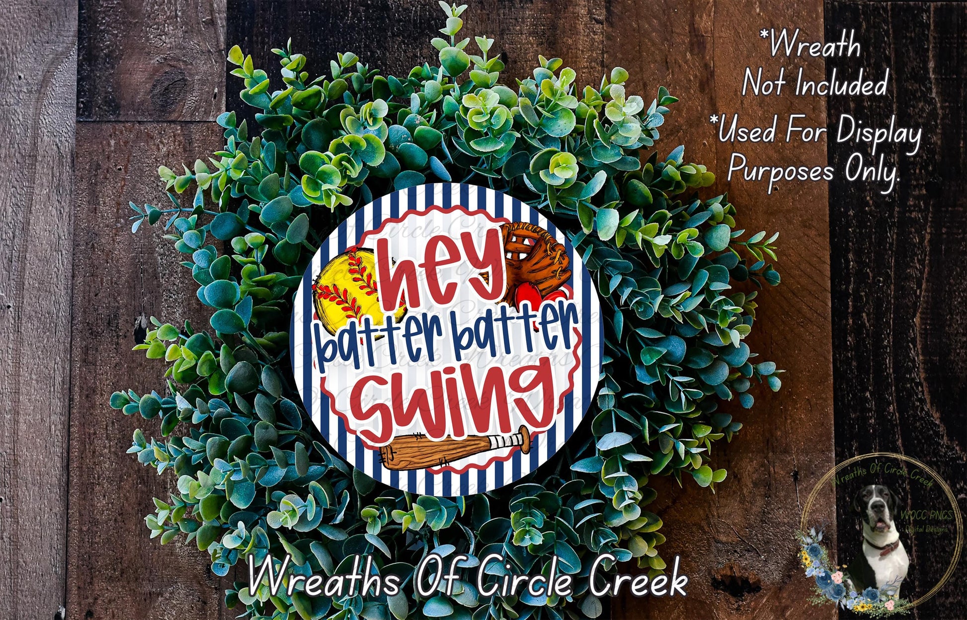 a wreath made of green leaves and a baseball-themed sign that says "hey batter batter swing". The sign is surrounded by the wreath, which is placed on a wooden surface.
