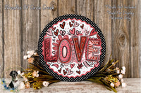 A decorative wreath with the word "LOVE" written on it, surrounded by flowers and placed on a wooden surface.