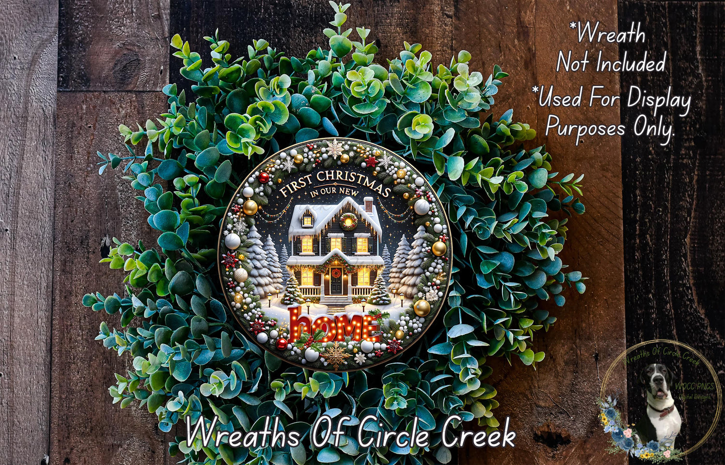 a Christmas wreath with a house and trees, surrounded by greenery. The wreath is displayed on a wooden surface, and there is a small dog in the bottom right corner of the image.