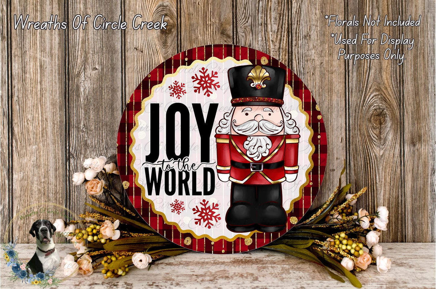 A decorative wreath with a nutcracker figure and the text "Joy to the World" on it, surrounded by flowers and placed on a wooden surface.