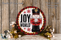 A decorative wreath with a nutcracker figure and the text "Joy to the World" on it, surrounded by flowers and placed on a wooden surface.