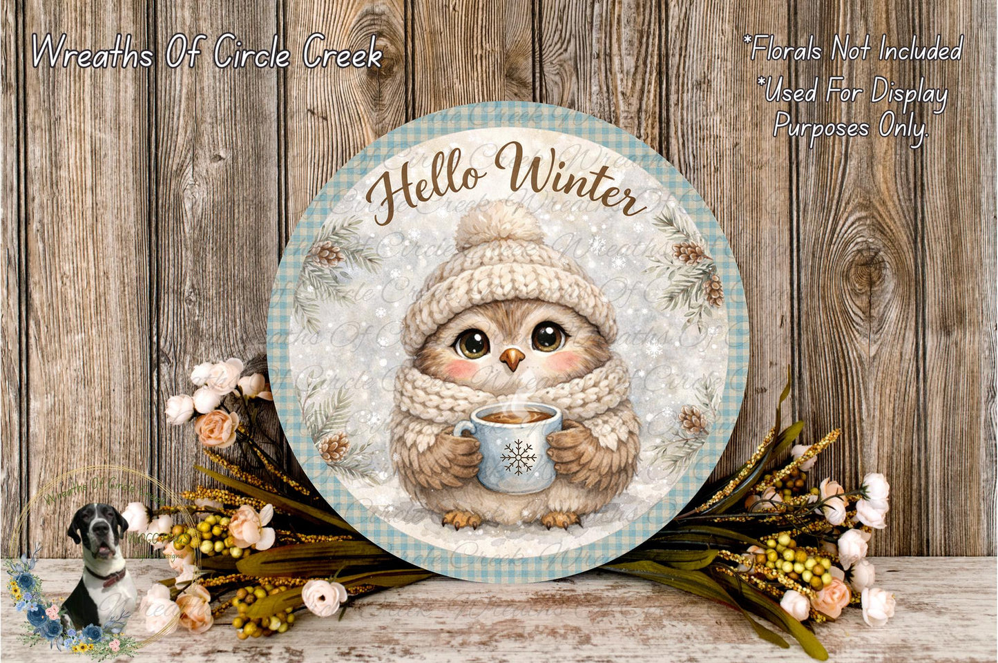 A round sign with a cartoon owl wearing a winter hat and scarf, holding a mug of hot chocolate, surrounded by flowers and a wooden background.