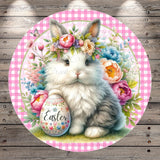 A white rabbit wearing a flower crown sits on a grassy surface, holding a decorated Easter egg.