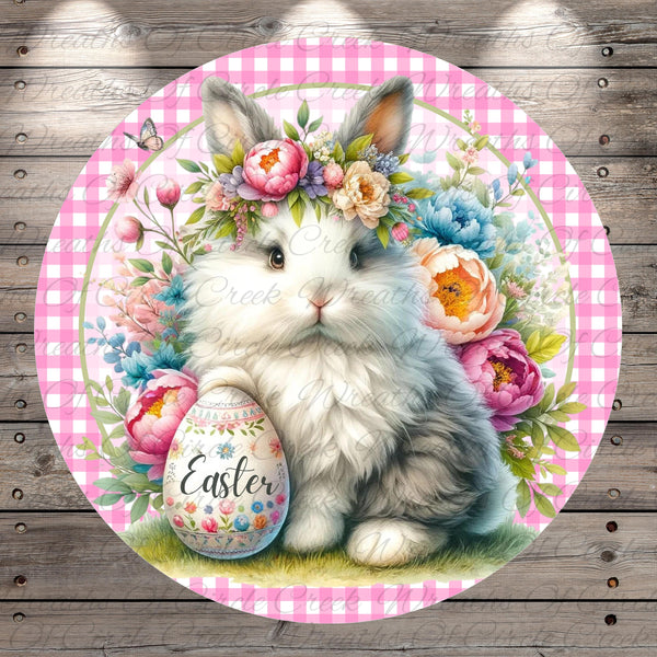A white rabbit wearing a flower crown sits on a grassy surface, holding a decorated Easter egg.
