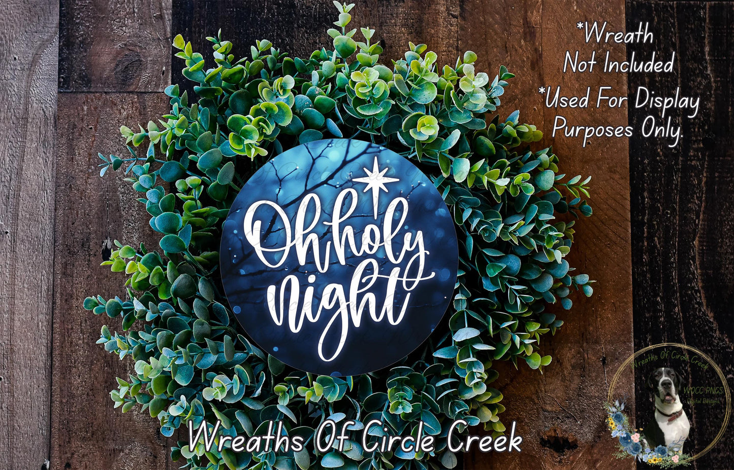 A wreath made of green leaves and a blue circular sign with the text "Oh holy night" is displayed on a wooden surface.