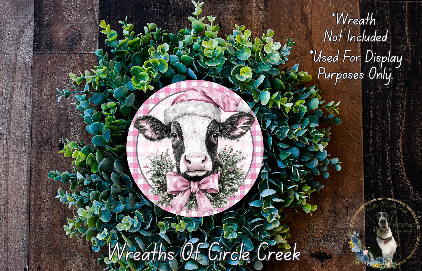 a wreath with a cow wearing a pink hat, surrounded by green foliage. The wreath is displayed on a wooden surface, and there is a text overlay that reads "Wreath Not Included * Used For Display Purposes Only" and "Wreaths of Circle Creek".