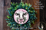 a wreath with a cow wearing a pink hat, surrounded by green foliage. The wreath is displayed on a wooden surface, and there is a text overlay that reads "Wreath Not Included * Used For Display Purposes Only" and "Wreaths of Circle Creek".