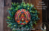 A wreath made of green leaves and flowers, with a colorful turkey decoration in the center.