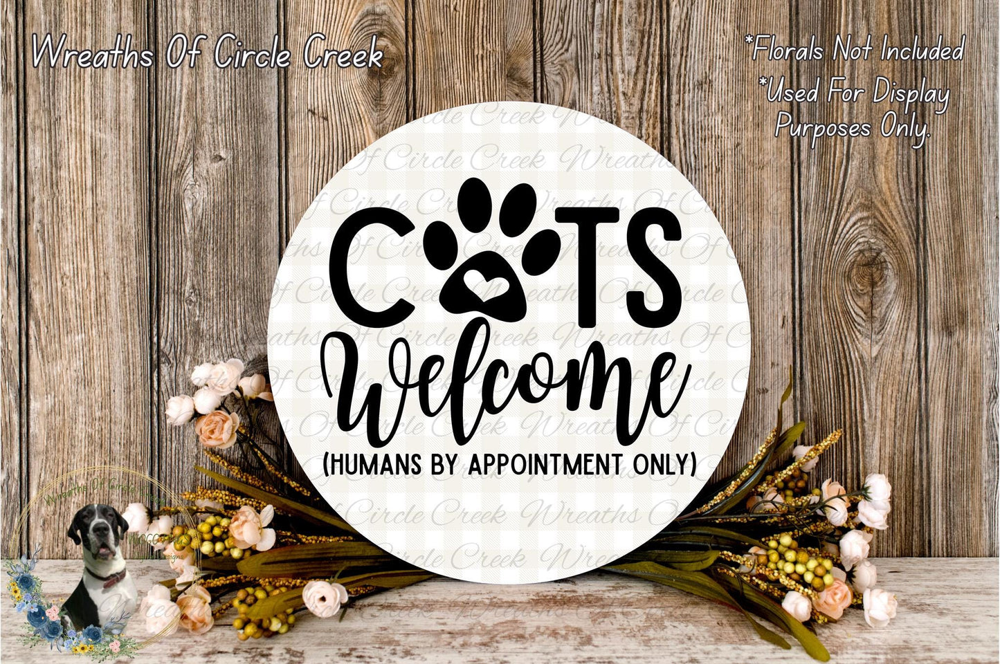 a circular sign with the text "CATS WELCOME (HUMANS BY APPOINTMENT ONLY)" surrounded by a floral arrangement and a wooden background.