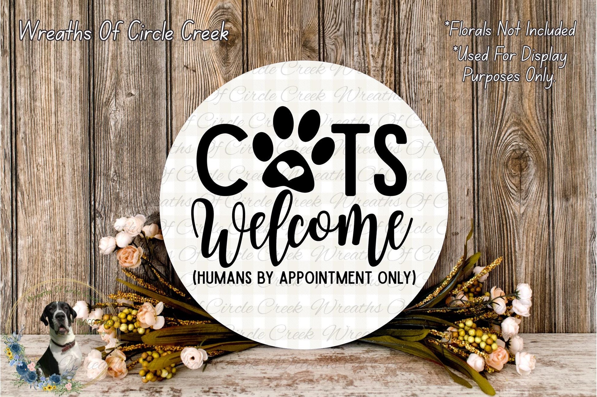 a circular sign with the text "CATS WELCOME (HUMANS BY APPOINTMENT ONLY)" surrounded by a floral arrangement and a wooden background.