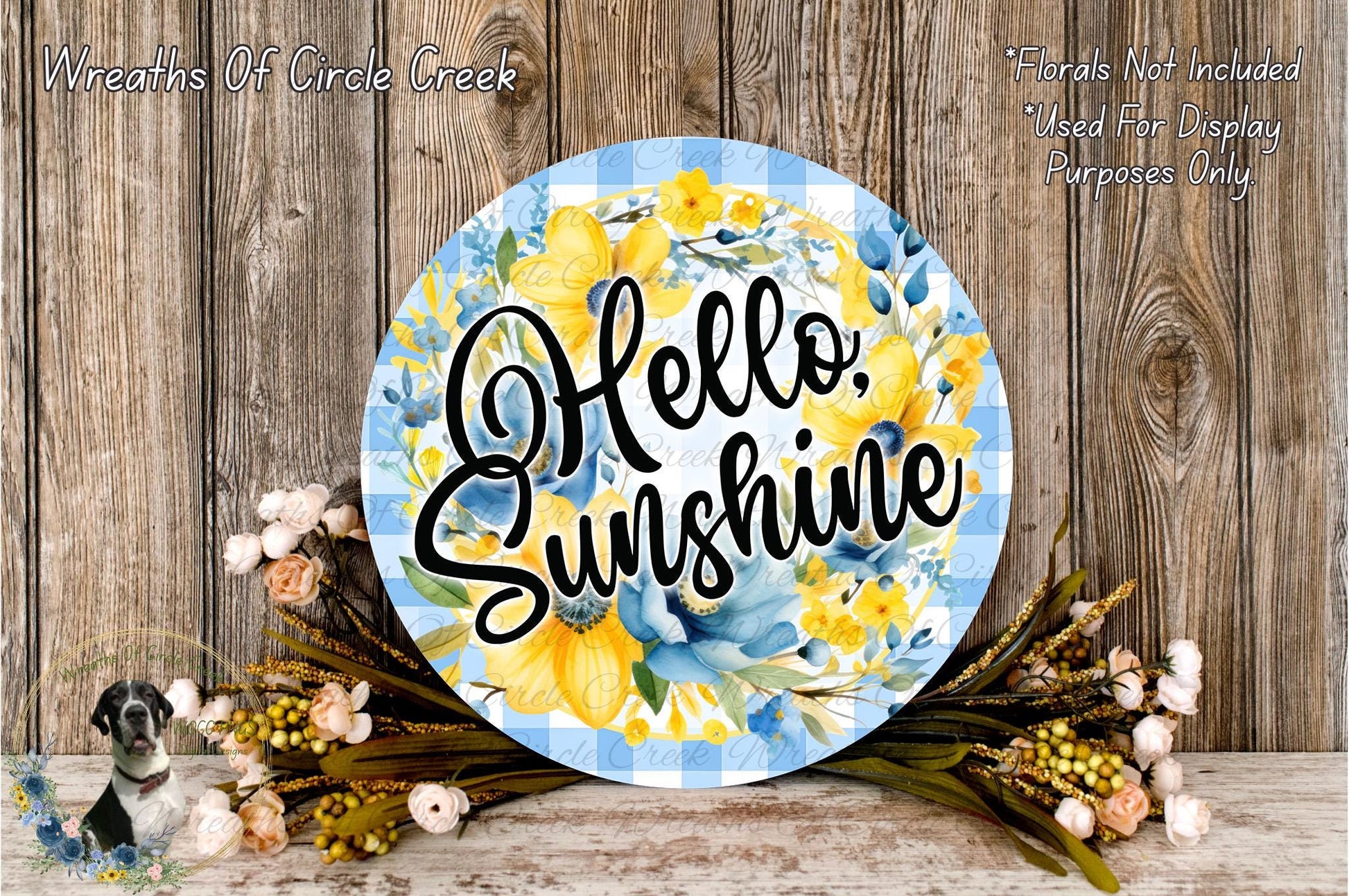 a round sign with the text "Hello. Sunshine" written on it, surrounded by a floral arrangement and some flowers.