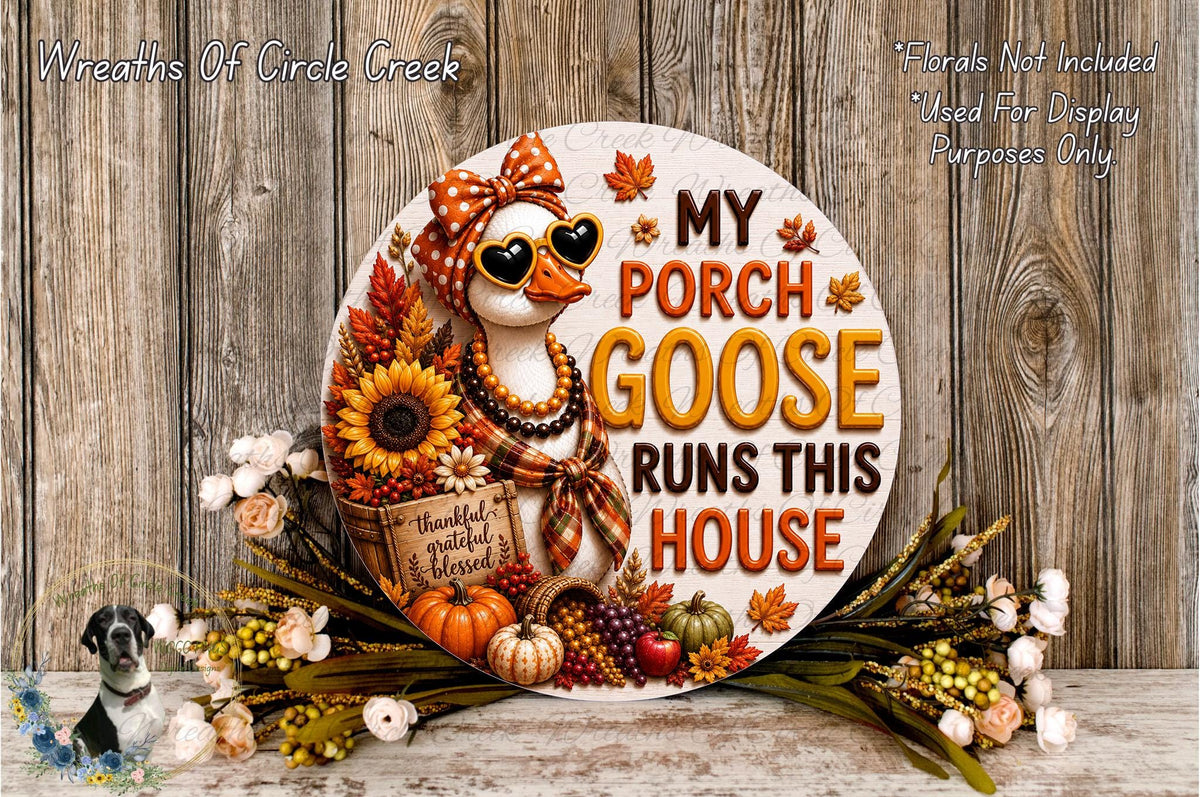 A decorative sign featuring a goose wearing sunglasses and surrounded by autumn-themed elements such as sunflowers, pumpkins, and leaves. The sign has the text "My Porch Goose Runs This House" and is displayed on a wooden surface.