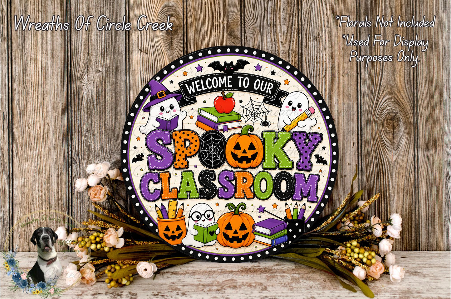 a Halloween-themed sign that reads "Welcome to our Spooky Classroom" with various Halloween-related elements such as a ghost, a witch's hat, a jack-o-lantern, and a spider web. The sign is surrounded by a floral arrangement and a wooden background, creating a festive and spooky atmosphere.