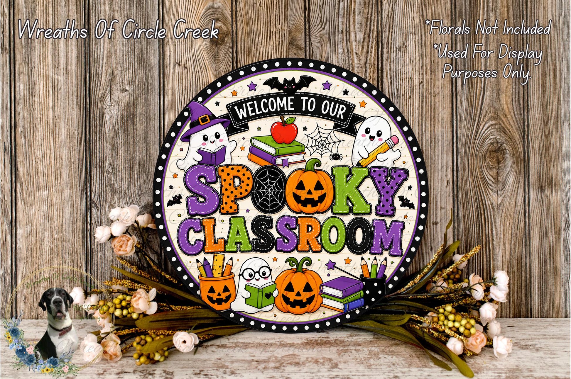 a Halloween-themed sign that reads "Welcome to our Spooky Classroom" with various Halloween-related elements such as a ghost, a witch's hat, a jack-o-lantern, and a spider web. The sign is surrounded by a floral arrangement and a wooden background, creating a festive and spooky atmosphere.