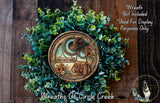 a wreath with a cowboy hat and a bag, surrounded by greenery, placed on a wooden surface.