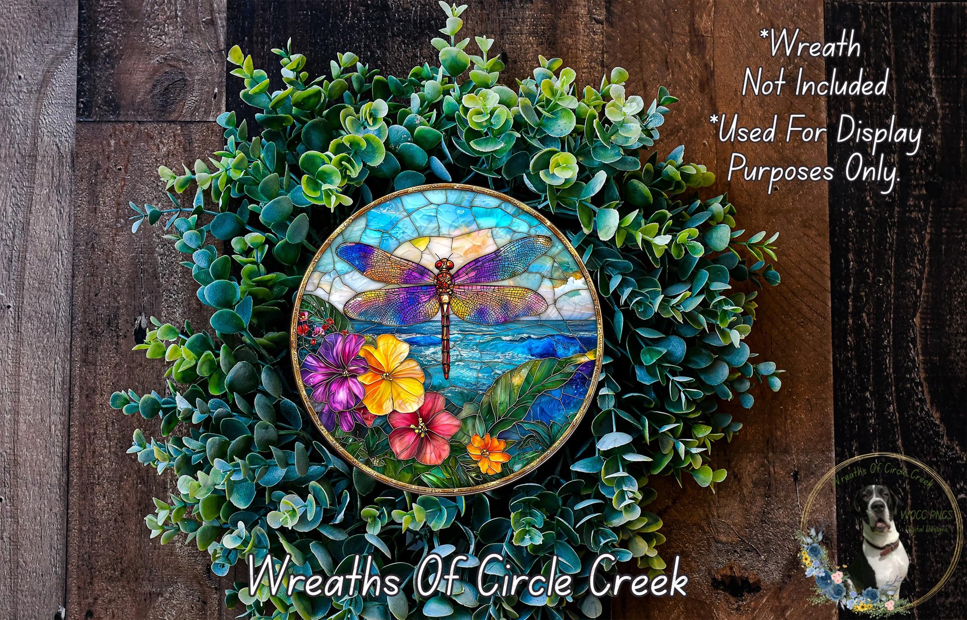 A colorful stained glass-style dragonfly is displayed on a wreath made of green foliage and flowers, with a wooden background.