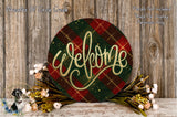 a circular welcome sign with a plaid pattern and the word "Welcome" written on it, placed on a wooden surface. There are also some flowers and greenery surrounding the sign.