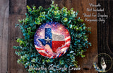A wreath made of greenery and featuring a Texas state flag design, with a fireworks display in the background.