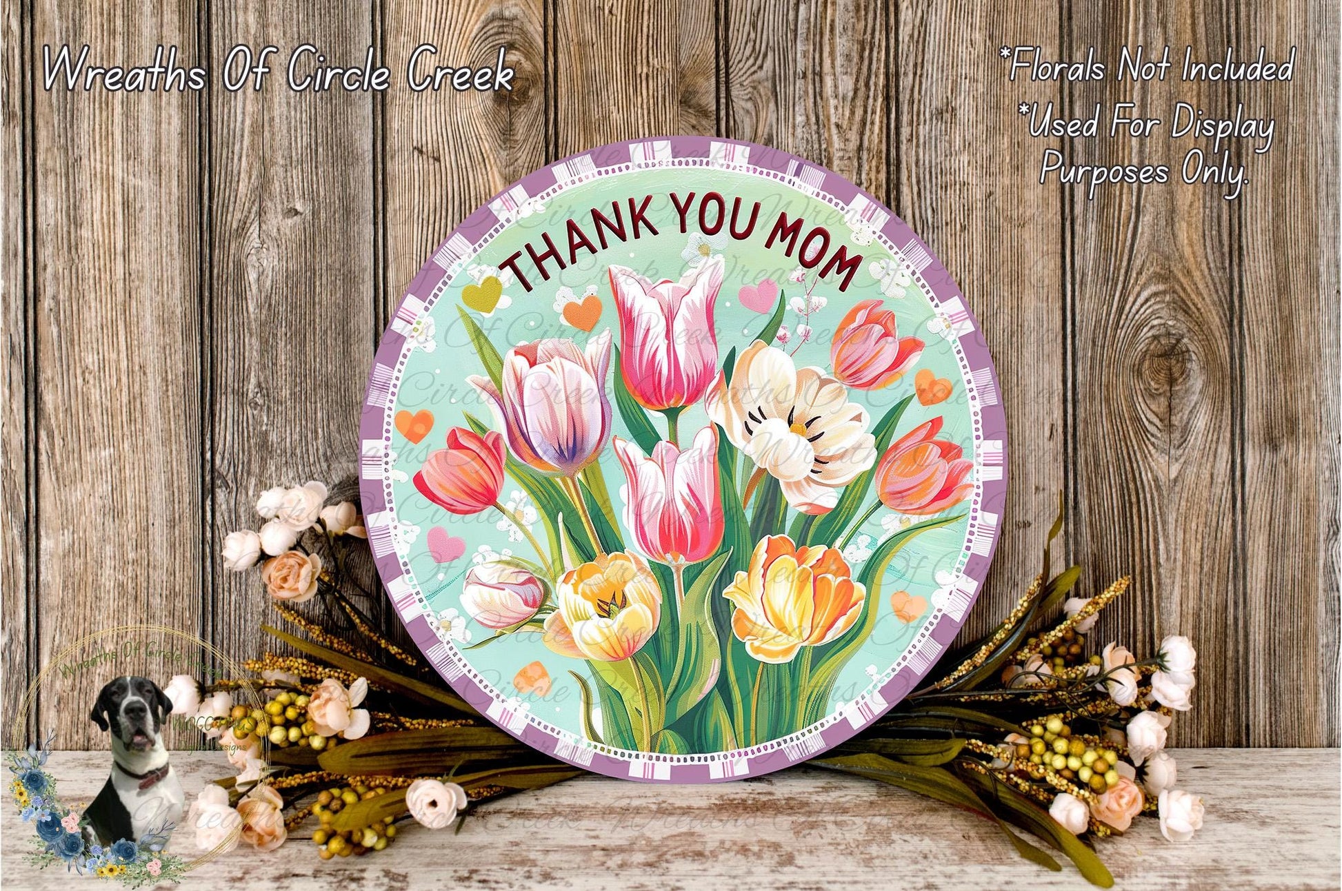 a round sign with a floral design, surrounded by a bouquet of flowers and placed on a wooden surface.