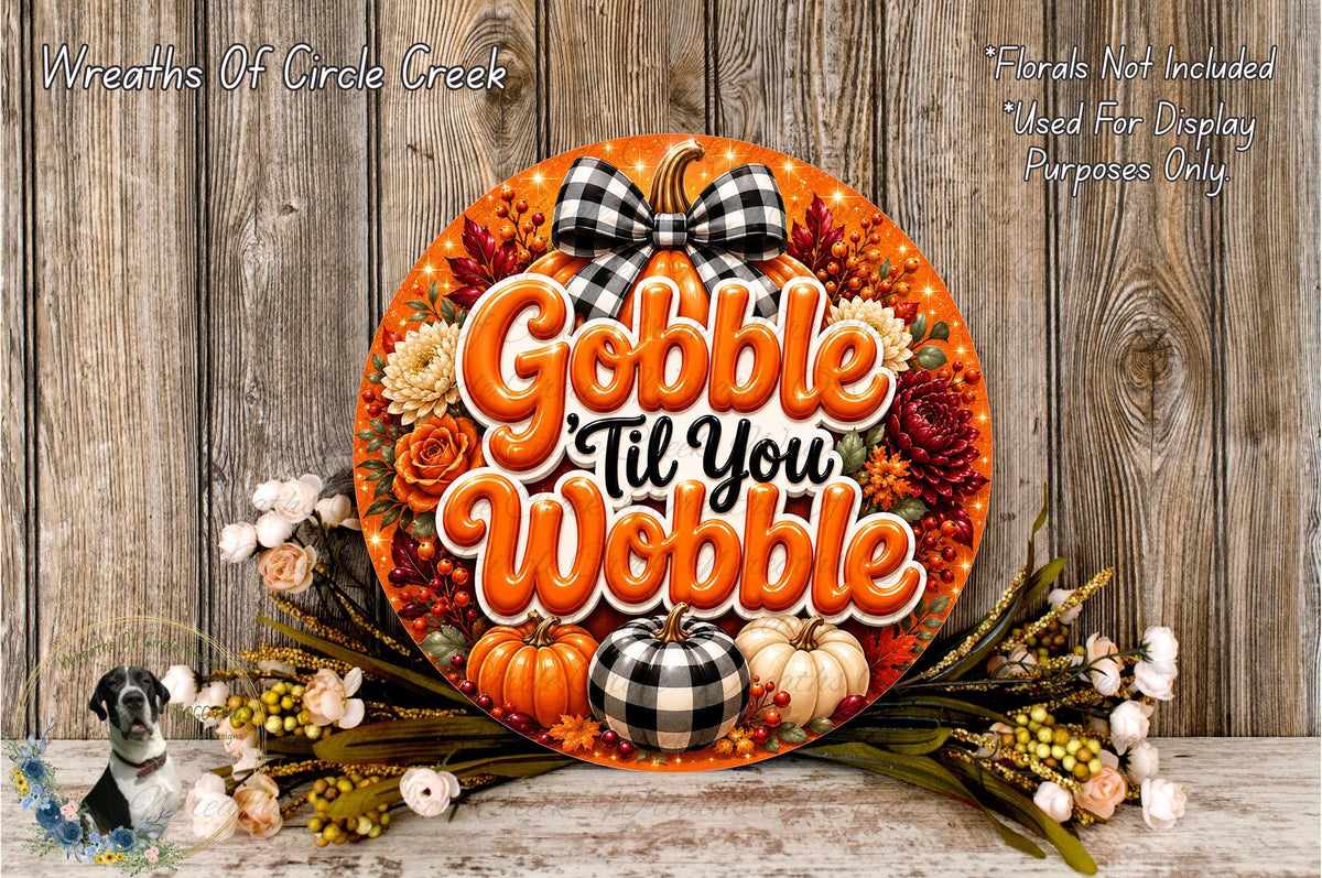 A decorative wreath with the text "Gobble 'til You Wobble" and various fall-themed elements such as pumpkins, flowers, and a bow. The wreath is displayed on a wooden surface, surrounded by additional fall-themed decorations.