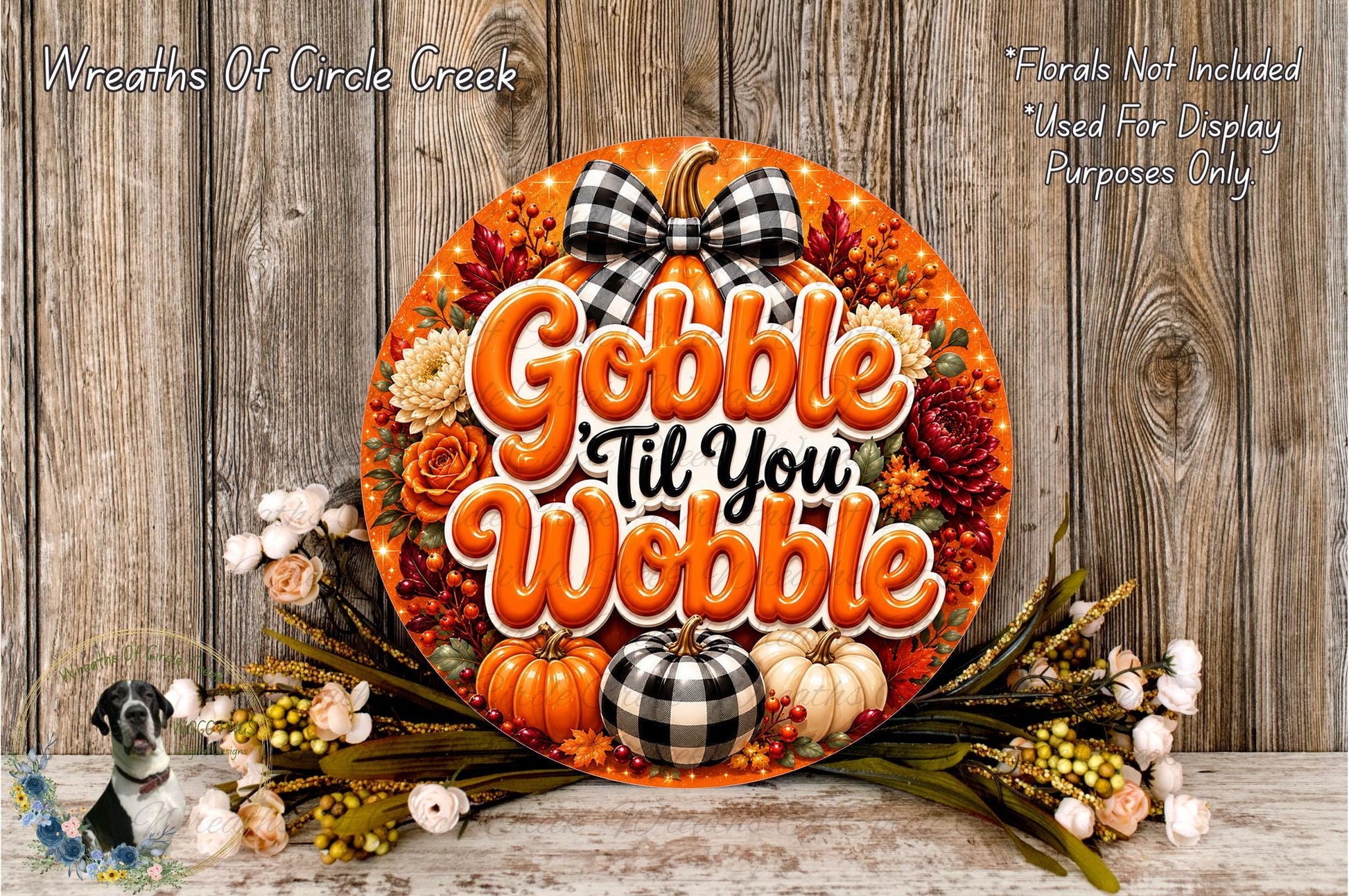 A decorative wreath with the text "Gobble 'til You Wobble" and various fall-themed elements such as pumpkins, flowers, and a bow. The wreath is displayed on a wooden surface, surrounded by additional fall-themed decorations.